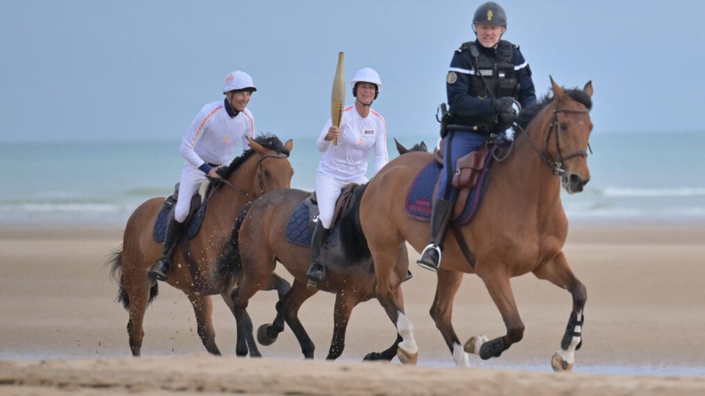 French show jumping rider and Olympic champion Penelope Leprevost (C) carries the Olympic flame on horseback, flanked by French impressionist Nicolas Canteloup (L) and mounted gendarmes, during the equestrian team's Olympic Relay, ahead of the Paris 2024 Olympic and Paralympic Games, on 