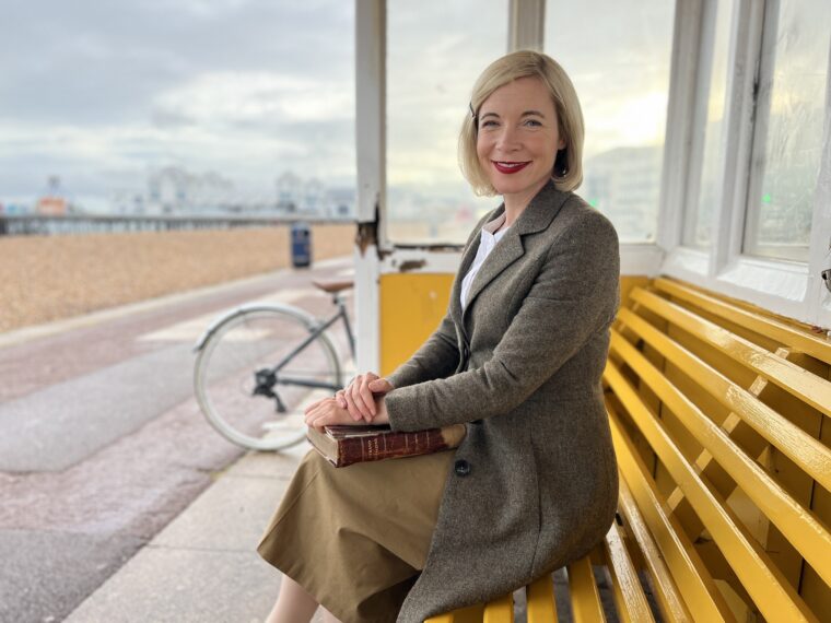 Lucy Worsley in Portsmouth Beach Shelter with book in hand