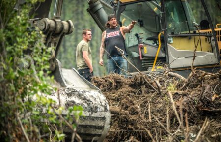 Rick Ness and Bailey Carten mid conversation by excavator, busy foreground in Gold Rush